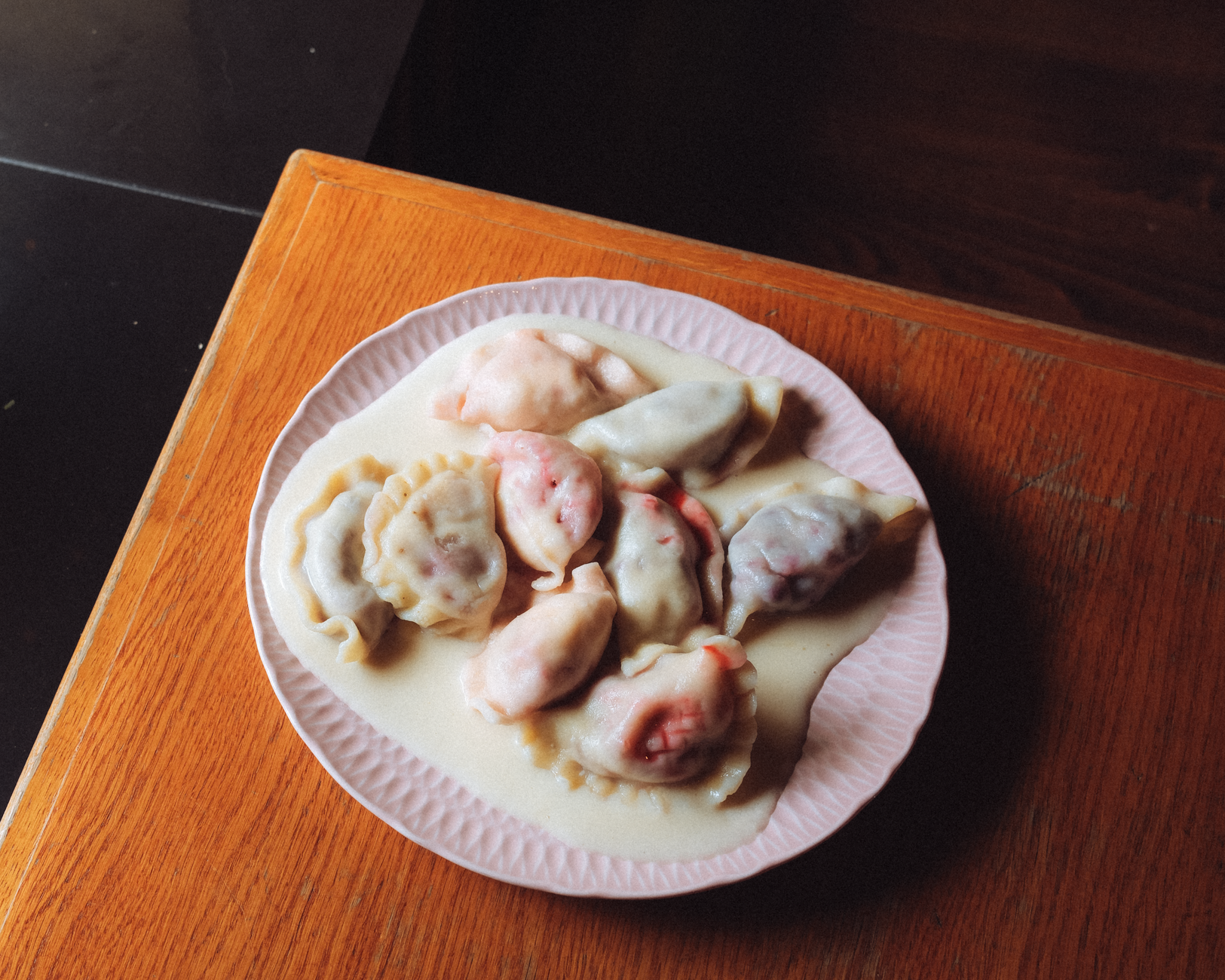 Talerz kolorowych pierogów w kremowym sosie na drewnianym stole