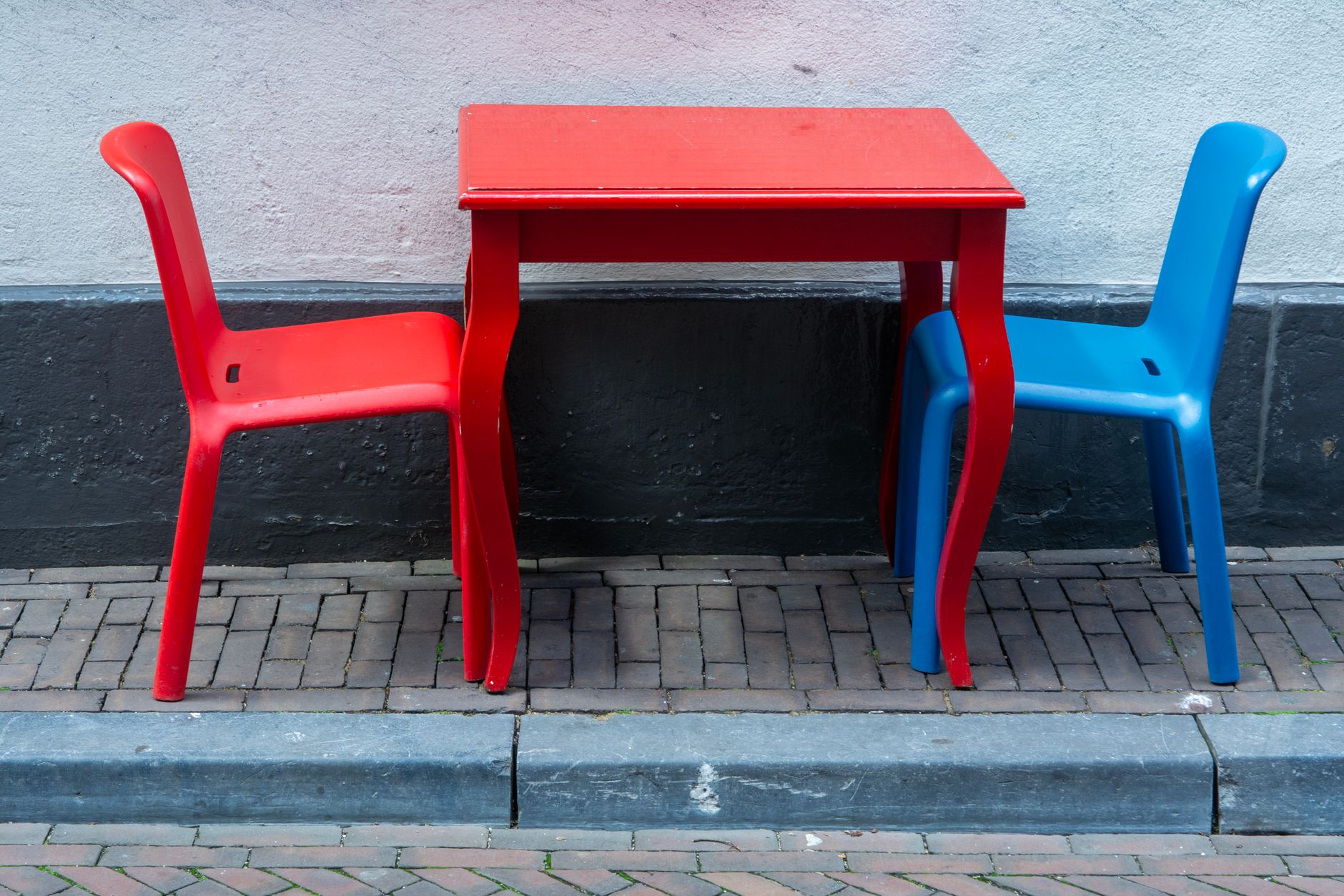 Czerwony stolik i plastikowe czerwone oraz niebieskie krzesła na chodniku